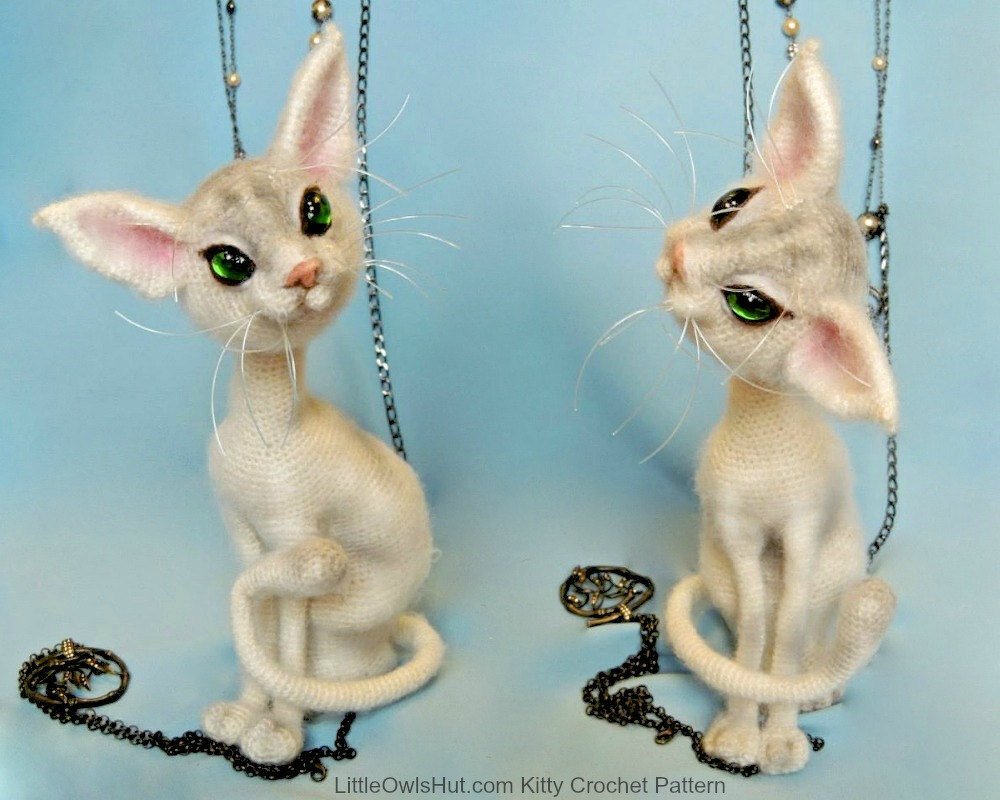 Two cream crocheted amigurumi cats with green eyes and curled tails