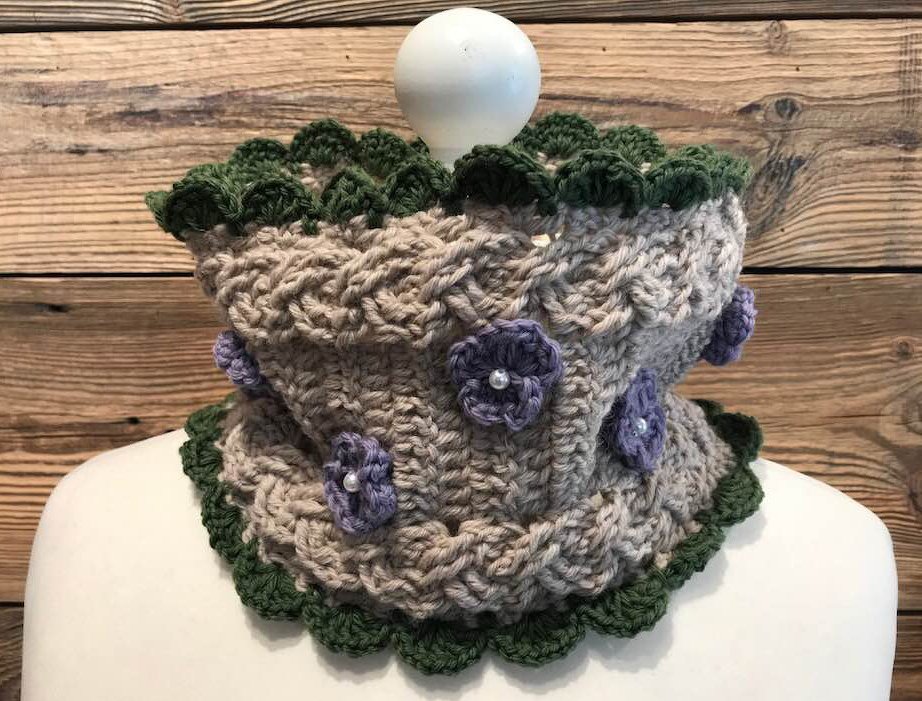 Beiger gehäkelter Loop mit grüner Muschelkante und lila Blüten