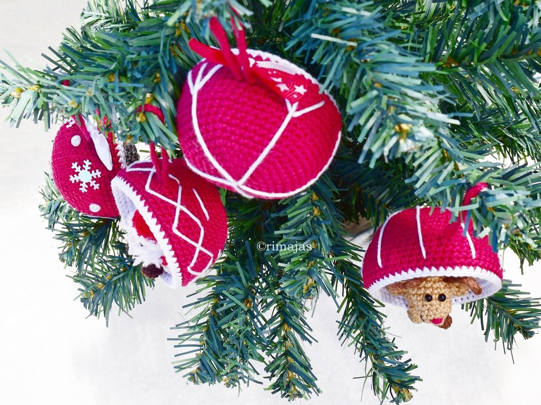 Nahaufnahme handgehäkelter roter und weißer Weihnachtsanhänger, darunter Rentier und Weihnachtsmann, an einem Tannenzweig