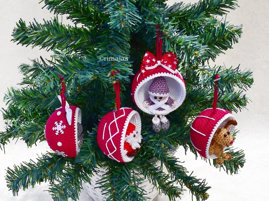 Rote und weiße gehäkelte Weihnachtskugeln mit kleinen Figuren (Wichtel, Weihnachtsmann, Rentier) an einem Tannenzweig