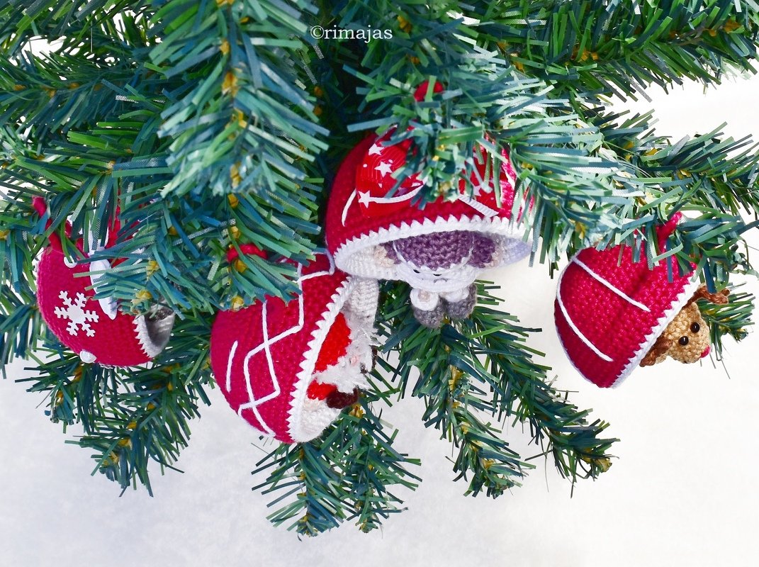 Rote gehäkelte Weihnachtskugeln, halb geöffnet, mit kleinen Amigurumi-Figuren an einem Tannenzweig