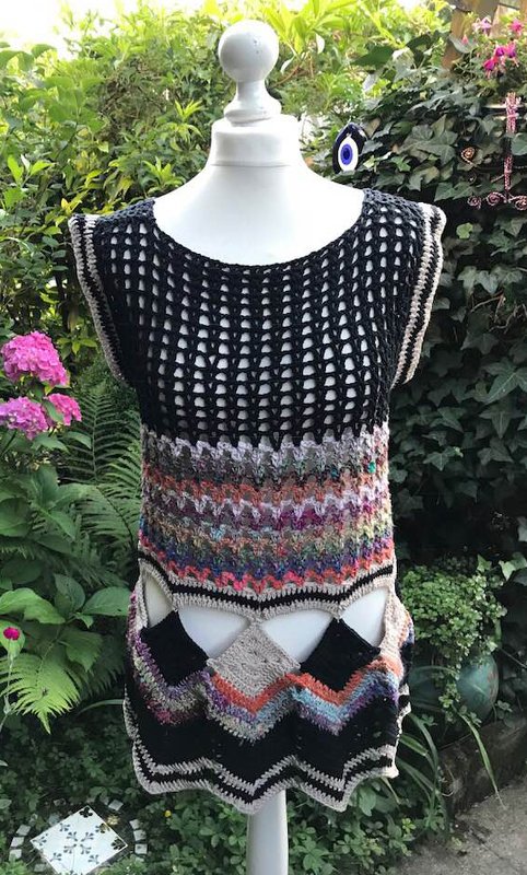 Ärmelloses gehäkeltes Damen-Top mit schwarzer Netzstruktur oben und mehrfarbigem Zickzackmuster unten auf einer Schaufensterpuppe im Garten.
