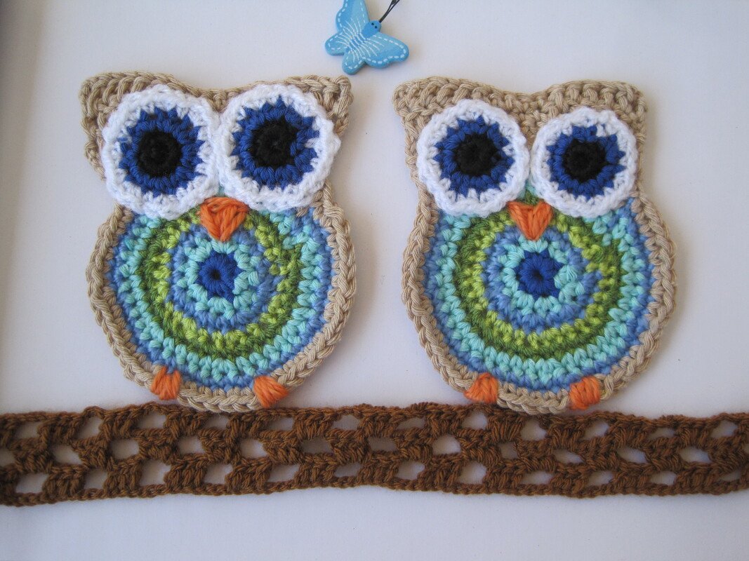 Zwei gehäkelte Eulen-Applikationen in Blau-Grün mit großen weißen Augen und orangefarbenen Details