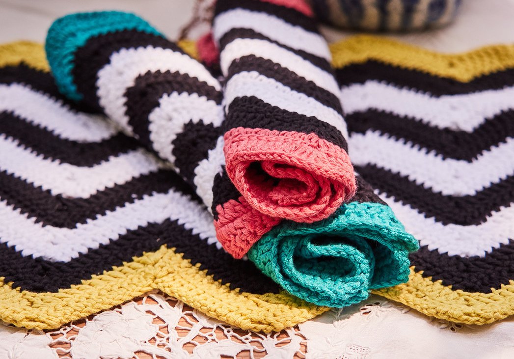 Gehäkelte Tücher mit Schwarz‑Weiß‑Chevronmuster und farbigen Rändern auf einem Spitzentuch.