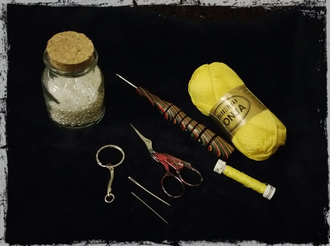 Knäuel gelbes Garn, Häkelnadel, kleine Schere, Stopfnadeln, Glas mit Perlen und Schlüsselring