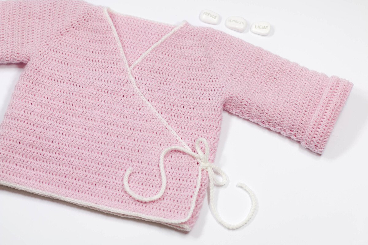 Rosa gehäkelte Baby-Wickeljacke mit weißer Einfassung und Bindeband