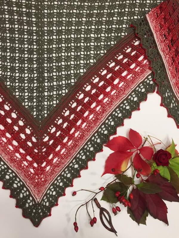 Red and olive green crocheted triangle shawl with lace pattern and scalloped edge, styled with autumn foliage.