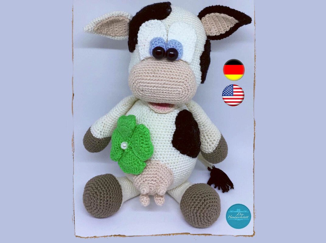 Hand-crocheted amigurumi cow with black spots and a green clover on its chest