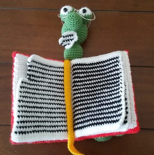 Gehäkelter grüner Lesewurm mit Brille und offenem schwarz-weiß gestreiftem Buch