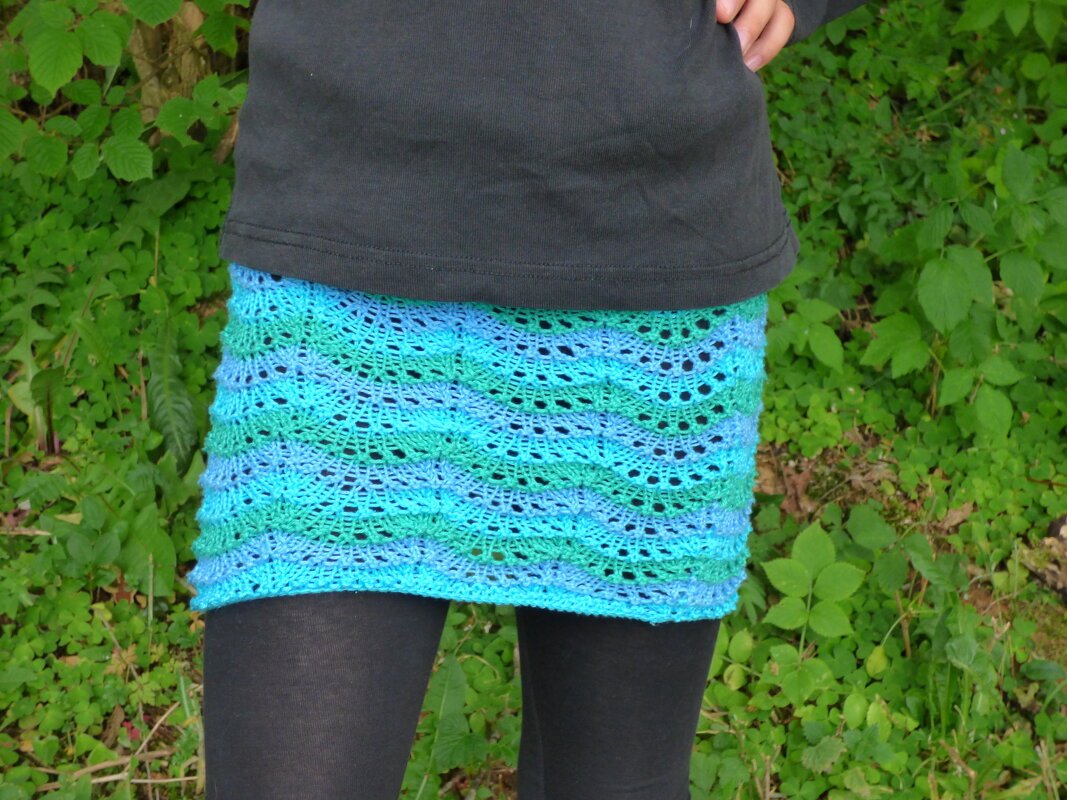 Gestrickter kurzer Rock in Blau- und Grüntönen mit Loch- und Wellenmuster über dunklen Leggings