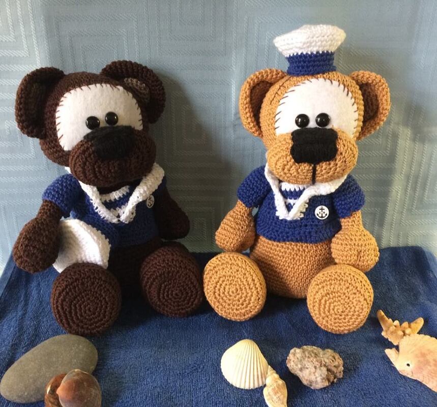 Zwei gehäkelte Amigurumi-Teddybären in blauen Matrosenhemden, einer mit Matrosenmütze, Muscheln im Vordergrund