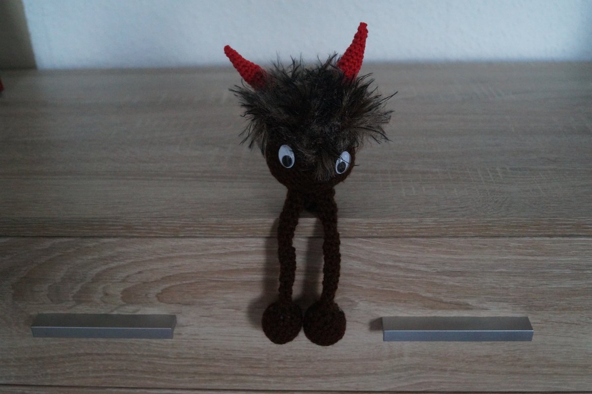 Braunes gehäkeltes Amigurumi mit roten Hörnern, flauschiger Kopfpartie und langen Beinen
