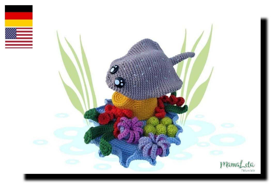 Gehäkelter grauer Amigurumi-Rochen mit großen Augen auf buntem Korallenriff