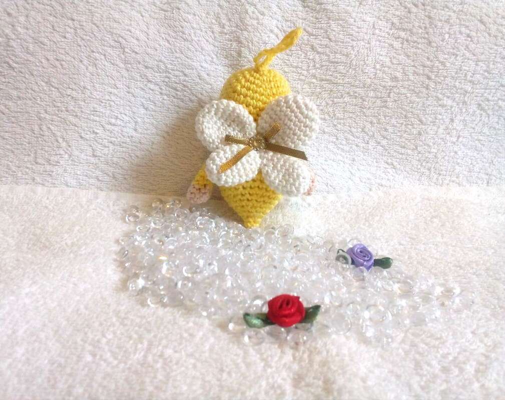 Kleiner Häkelengel in Gelb mit Aufhängeschlaufe, weißen Flügeln und Dekoperlen auf hellem Stoffhintergrund