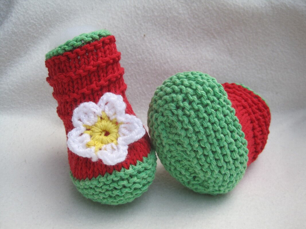 Handgestrickte Babyschuhe rot mit grünen Bündchen und weißer Blüte