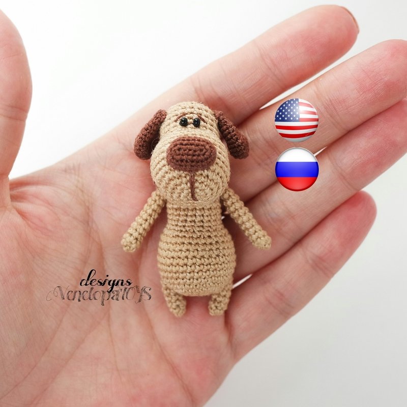 Small beige and brown crocheted amigurumi dog with floppy ears held in a hand