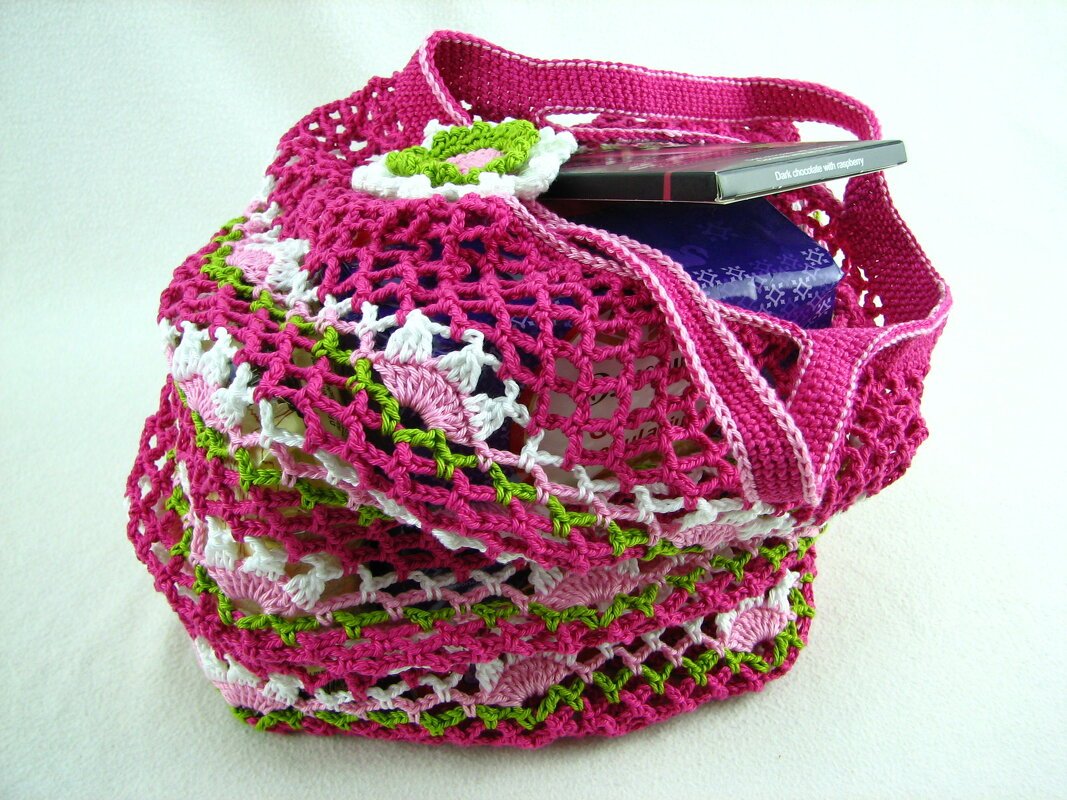 Gehäkelte pinke Henkeltasche mit weiß-grünem Netzmuster und Blumenapplikation, teils gefüllt
