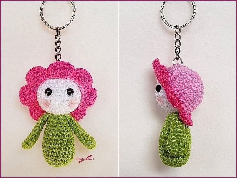 Gehäkelter Blumen-Amigurumi Schlüsselanhänger mit rosa Blüten, weißem Gesicht, schwarzen Augen und grünem Körper, am Metallring
