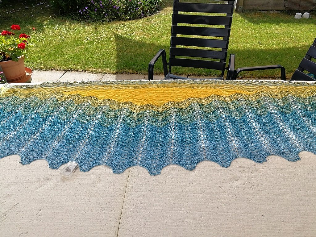 Gestricktes Wellentuch mit Gelb-Blau-Farbverlauf auf Terrasse ausgebreitet