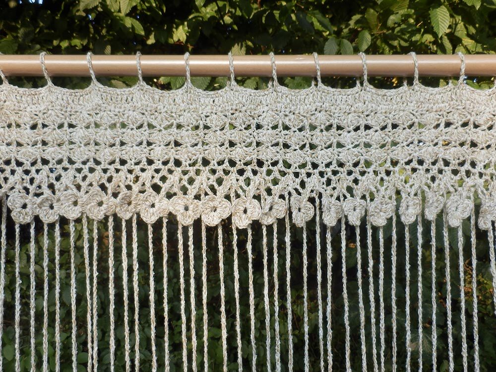 Beiger Häkelvorhang mit Aufhängeschlaufen, Blumenborte und langen Fransen an einer Holzstange