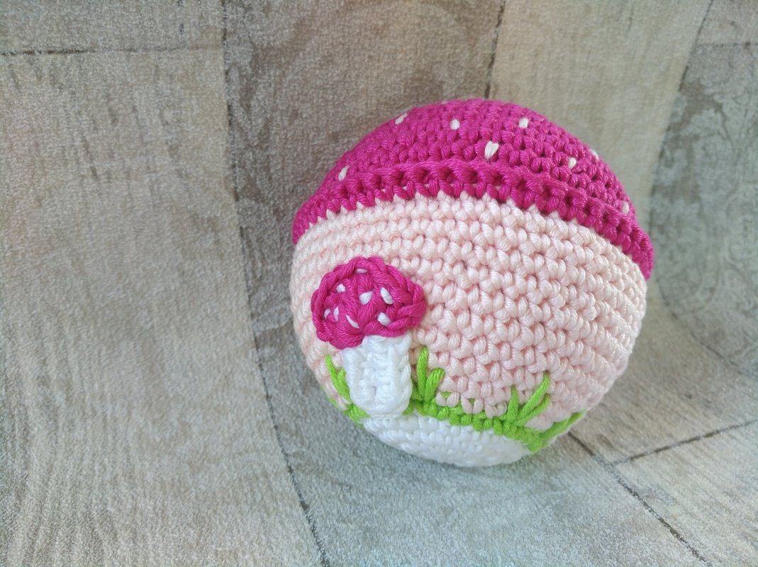 Gehäkelte rosa Baby-Greifkugel mit Pilz-Applikation und grünen Stichen
