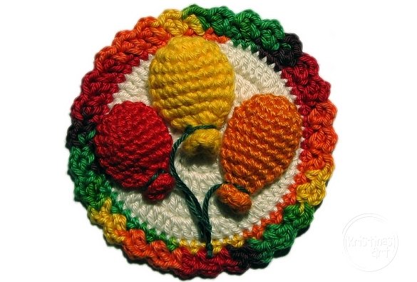 Runde gehäkelte Applikation mit drei plastischen Luftballons (Rot, Gelb, Orange) und mehrfarbigem Regenbogenrand auf weißem Hintergrund.