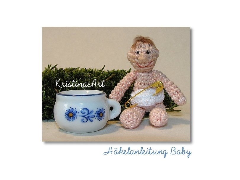 Gehäkelte Mini-Babypuppe mit weißer Windel und Sicherheitsnadel neben kleinem Porzellantässchen