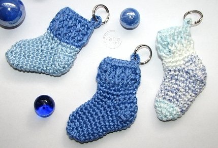 Drei gehäkelte Mini-Socken-Schlüsselanhänger in Blau- und Weißtönen auf hellem Untergrund.