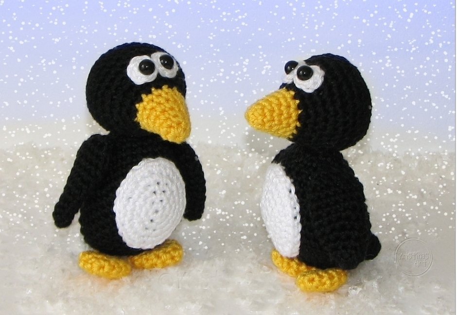 Zwei gehäkelte schwarze Pinguine mit weißen Bäuchen und gelben Schnäbeln im Schnee