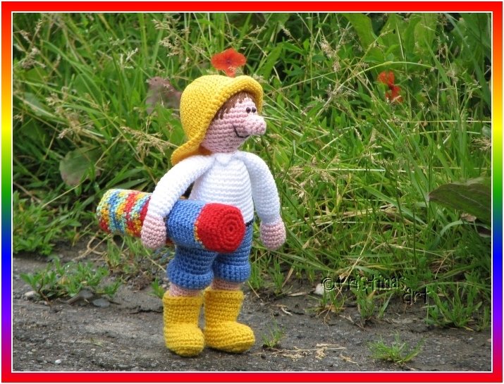 Gehäkelte Amigurumi-Puppe mit gelbem Hut und gerollter bunter Matte im Gras