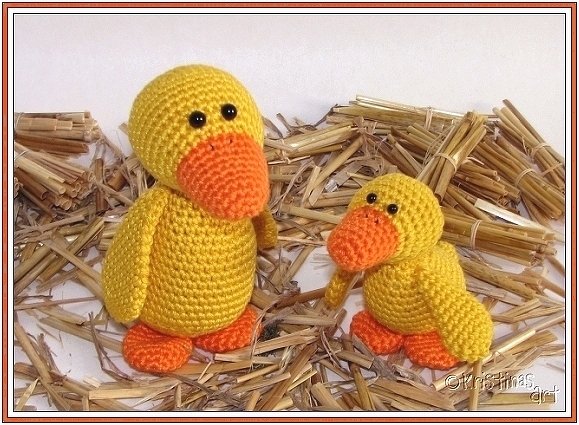 Gehäkelte gelbe Ente und kleines Küken nebeneinander auf Stroh