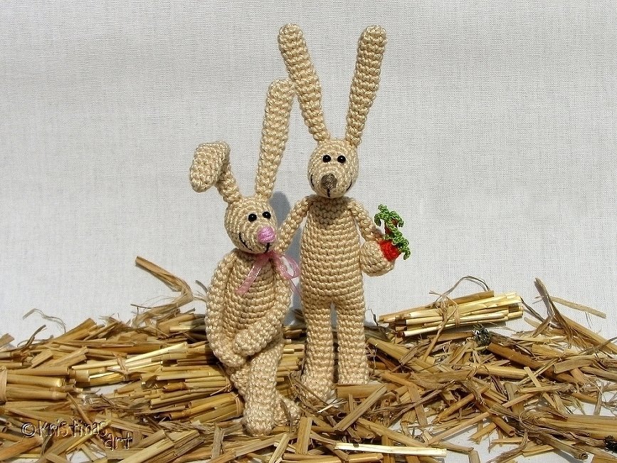 Zwei rustikale gehäkelte Osterhasen auf Stroh, einer hält eine Karotte
