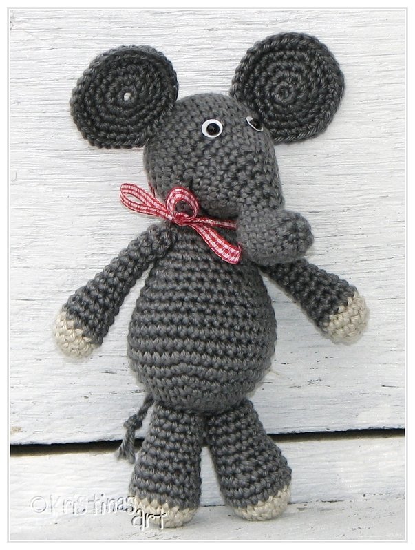 Gehäkelter grauer Amigurumi‑Elefant mit Kulleraugen, kariertem Schleifchen und hellen Pfoten auf hellem Holz.