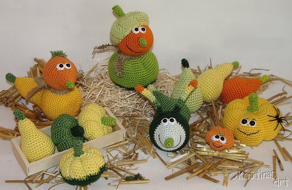 Mehrere gehäkelte Kürbisse und Zierkürbisse mit Gesichtern in Orange, Gelb und Grün auf Stroh