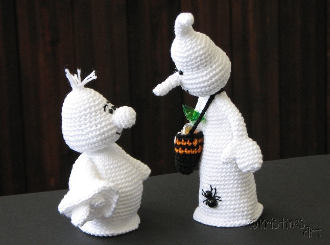 Zwei weiße gehäkelte Gespenster-Amigurumi auf dunklem Untergrund, eines mit Mini-Süßigkeitstasche und Spinnen-Applikation