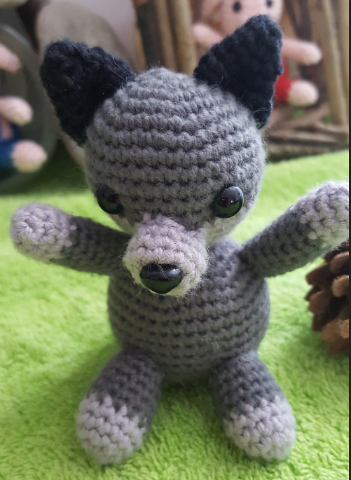 Kuscheliges graues Wolf-Amigurumi mit schwarzen Ohren, sitzend