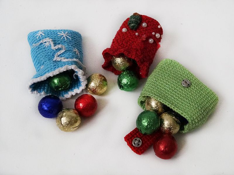 Drei gehäkelte Säckchen in Blau, Rot und Grün mit Schokokugeln auf weißem Hintergrund.