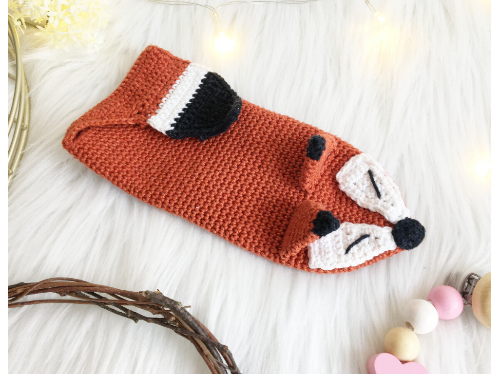 Gehäkeltes Fuchs-Utensilo in Rostbraun mit weißen und schwarzen Details auf hellem Felluntergrund