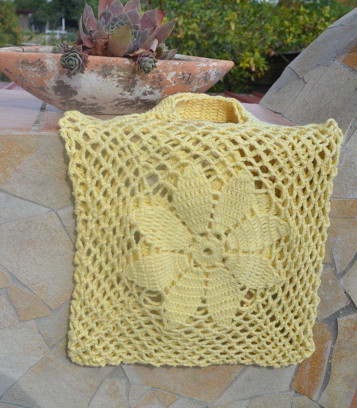 Hellgelbe gehäkelte Netztasche mit Blumenmotiv auf Fliesen neben Pflanztopf