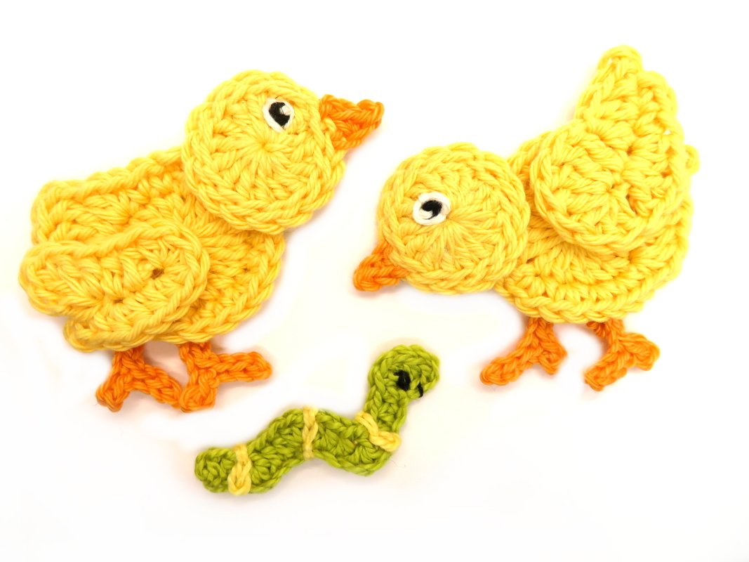 Two yellow crocheted chick appliques and one green crocheted worm applique on a white background.