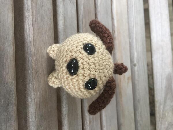 Beige crocheted amigurumi puppy head with brown ears and black safety eyes on wooden slats