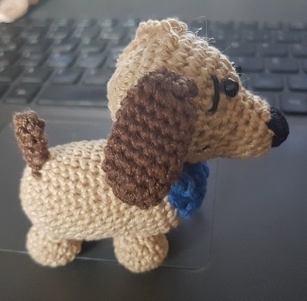 Beiger gehäkelter Amigurumi-Hund mit braunen Ohren und blauem Halsband auf Laptop-Tastatur