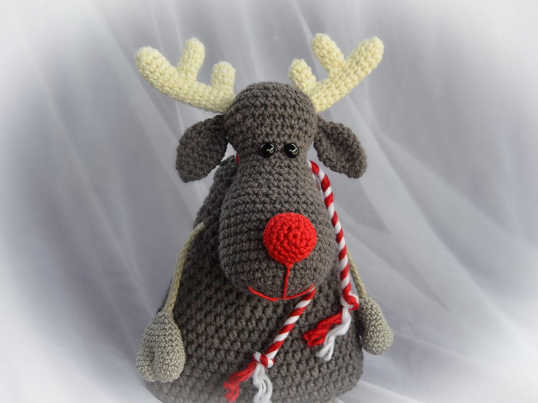 Gehäkeltes Rentier in Braun mit roter Nase, cremefarbenen Geweihen und rot-weiß gestreifter Kordel.