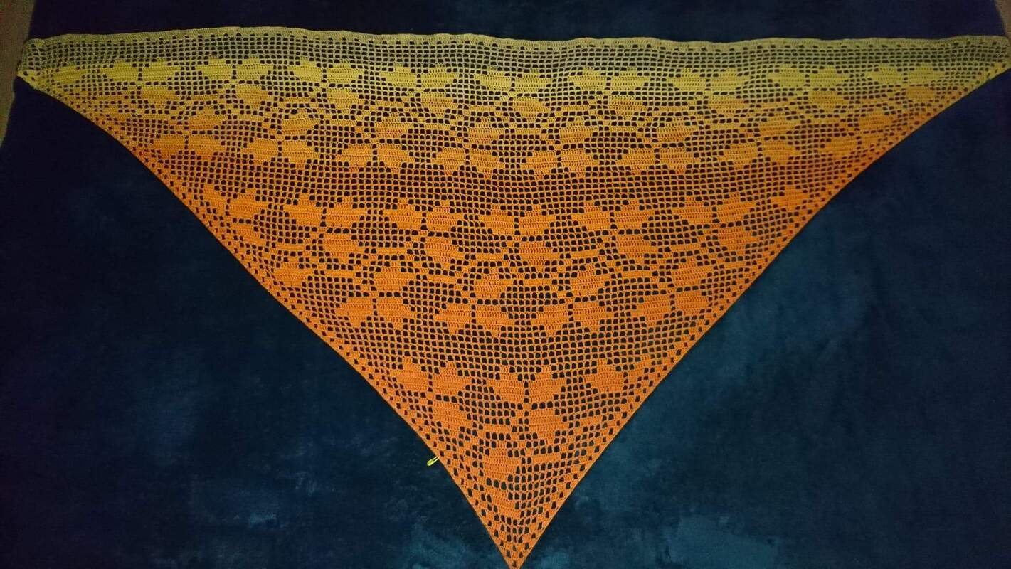Gehäkeltes Dreieckstuch in Gelb‑Orange mit Herzmuster auf dunklem Untergrund