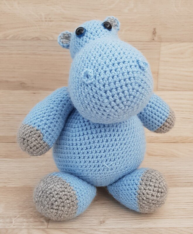 Hellblaues gehäkeltes Nilpferd-Amigurumi mit grauen Pfoten, sitzend