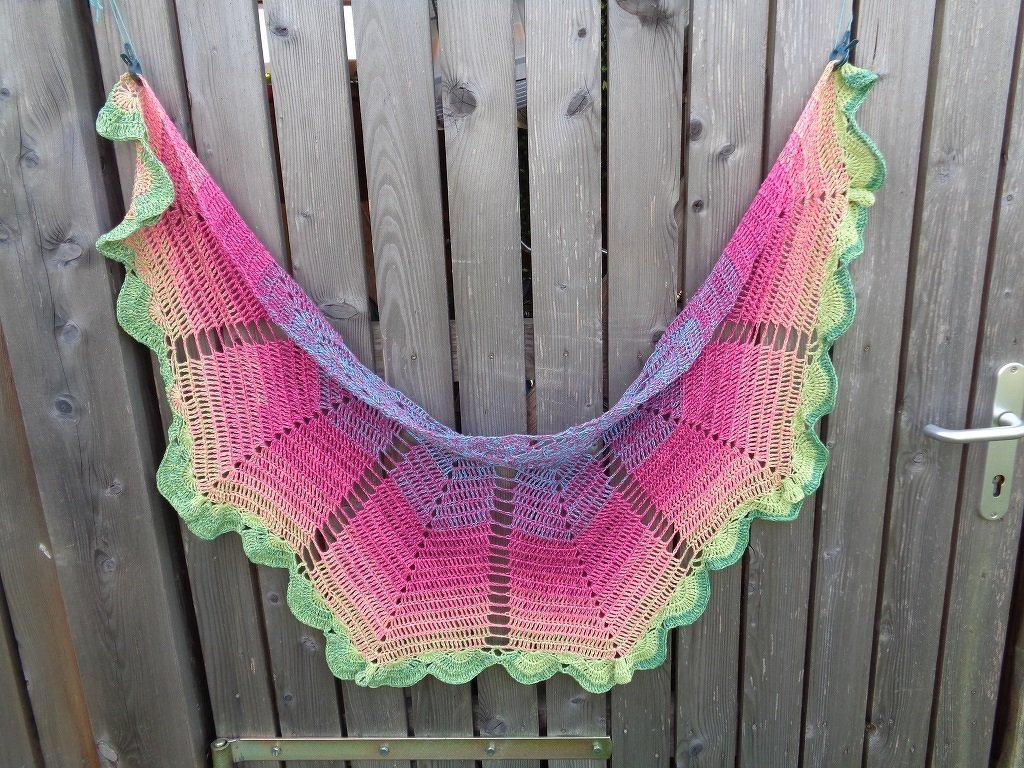 Halbrundes Häkeltuch in Pink, Orange und Grün mit Rüschenrand an Holzzaun