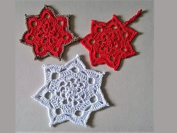 Drei gehäkelte sechszackige Sterne, zwei rot und einer weiß, auf hellem Hintergrund