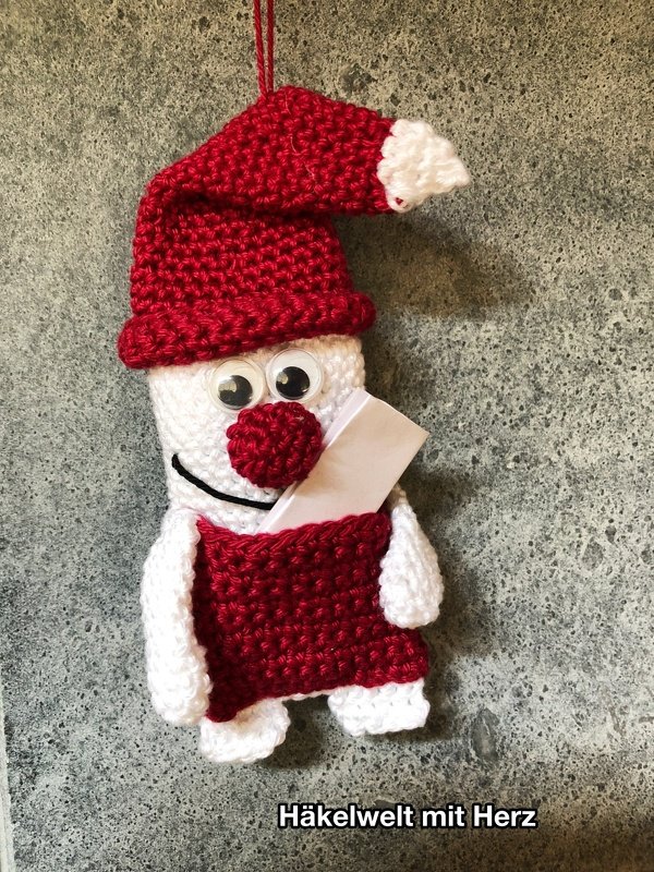 Gehäkelter Weihnachtsanhänger mit roter Mütze, Kulleraugen und kleiner Tasche