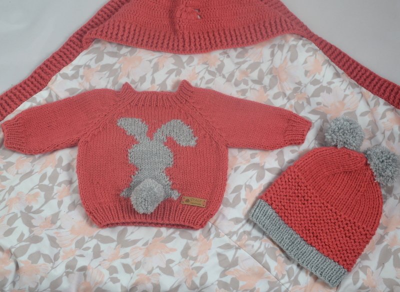 Gestricktes Baby-Set in Koralle und Grau mit Pullover (Hasenapplikation und Pompon), zweifarbiger Bommelmütze und Strickdecke.