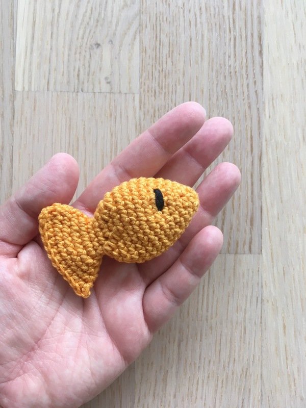 Hand hält kleinen gehäkelten gelb-orangefarbenen Fisch-Amigurumi